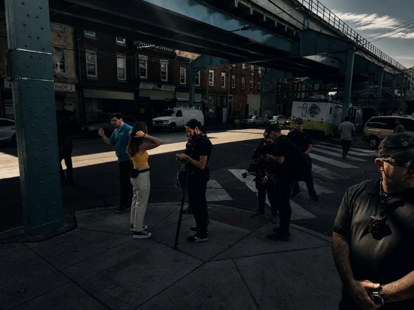 Security personnel supporting an urban media operation beneath an elevated rail line.